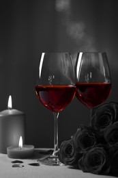 Image of Glasses of wine, burning candles and rose flowers for romantic dinner on grey table against blurred lights. Black and white effect with red accent