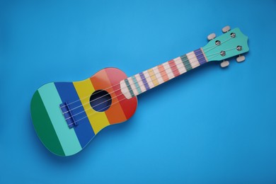 Photo of Colorful ukulele on light blue background, top view. String musical instrument