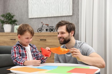 Photo of Dad and son making paper boats at coffee table indoors