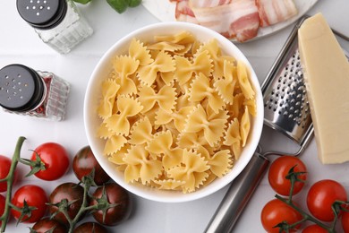 Photo of Raw pasta, bacon and fresh ingredients on white tiled table, flat lay