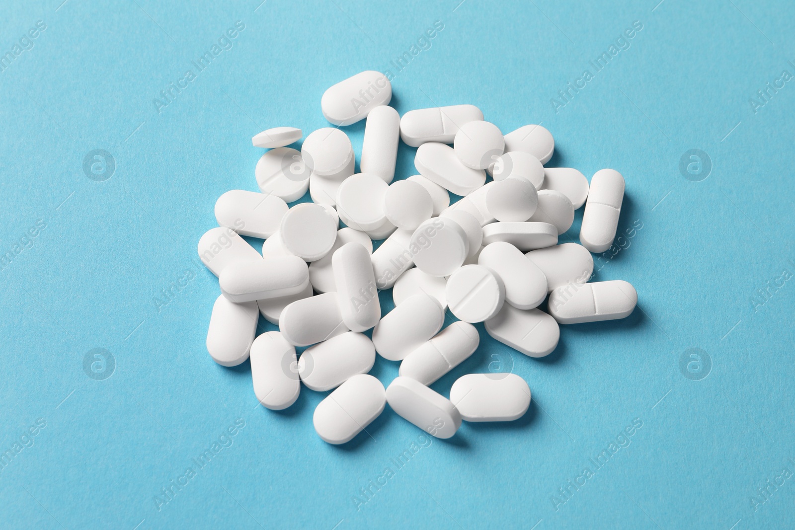 Photo of Pile of white pills on light blue background, above view