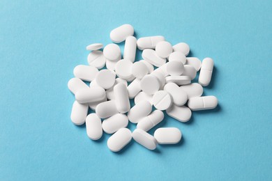 Pile of white pills on light blue background, above view