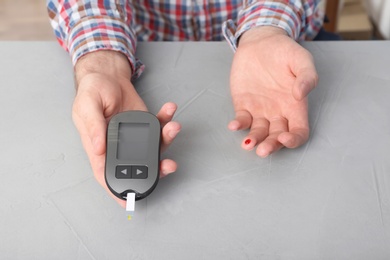 Man checking blood sugar level with glucometer at table. Diabetes test