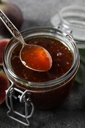 Photo of Spoon with tasty sweet jam over jar and fresh figs on grey table, closeup