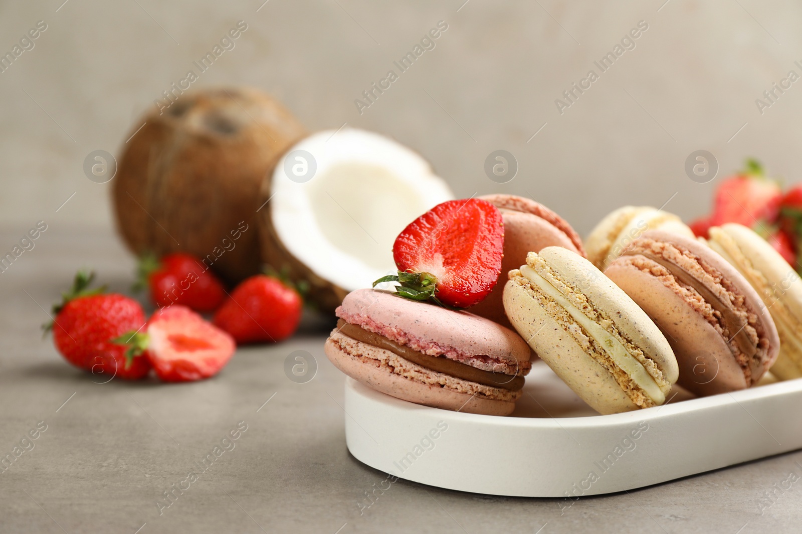 Photo of Delicious macarons, strawberries and coconut on grey table