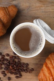 Coffee to go. Paper cup with tasty drink, croissants and beans on wooden table, flat lay