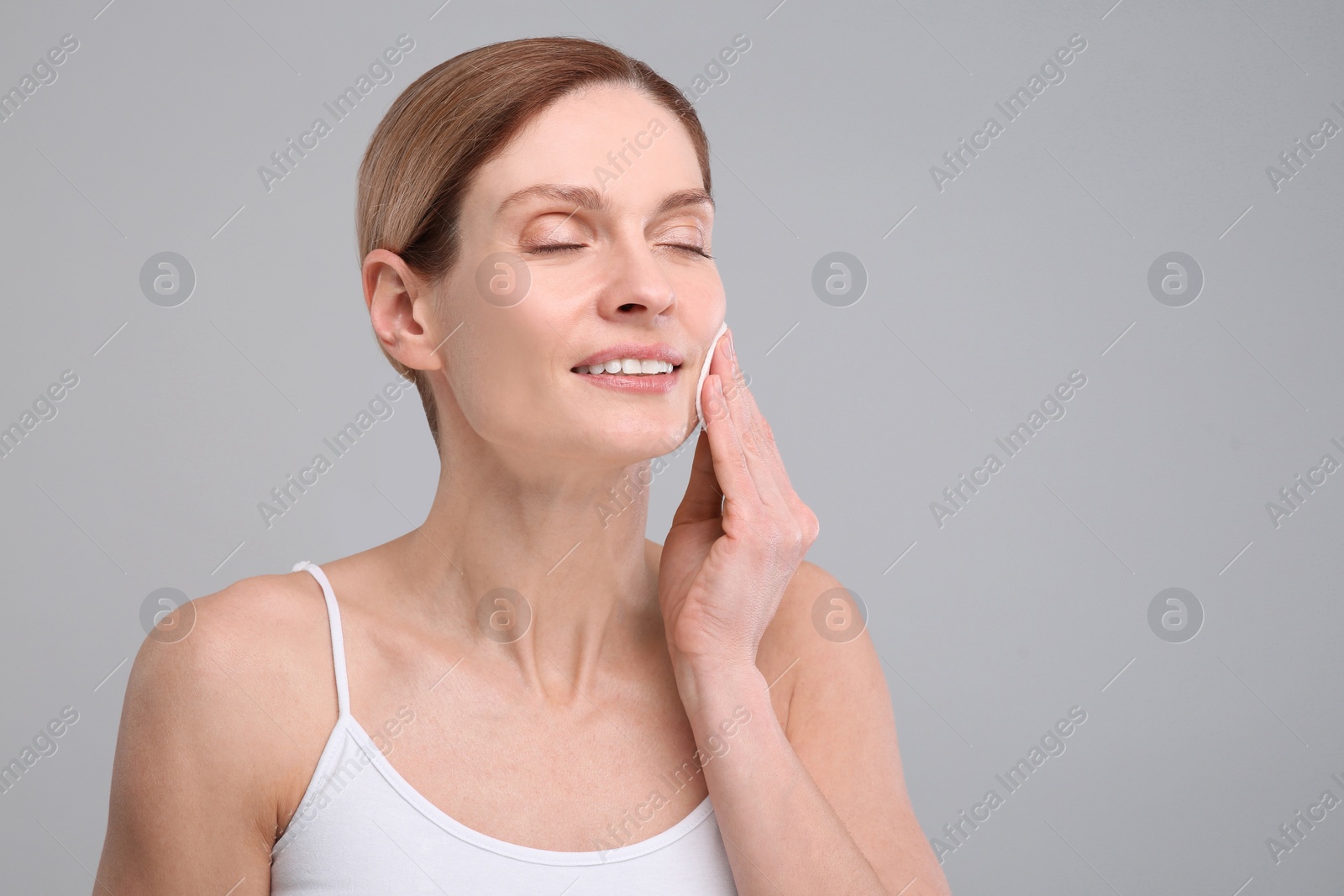 Photo of Beautiful woman removing makeup with cotton pad on gray background, space for text