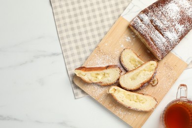 Pieces of delicious yeast dough cake and tea on white marble table, flat lay. Space for text