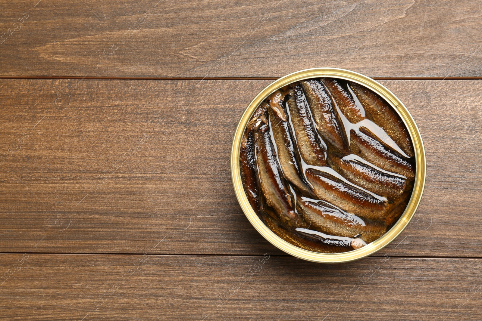 Photo of Sprats in tin can on wooden table, top view. Space for text