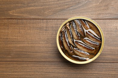 Sprats in tin can on wooden table, top view. Space for text