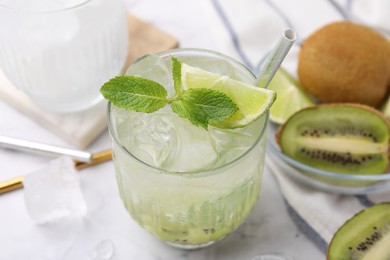 Photo of Glass of refreshing drink with lime, mint and cut kiwi on white table, closeup