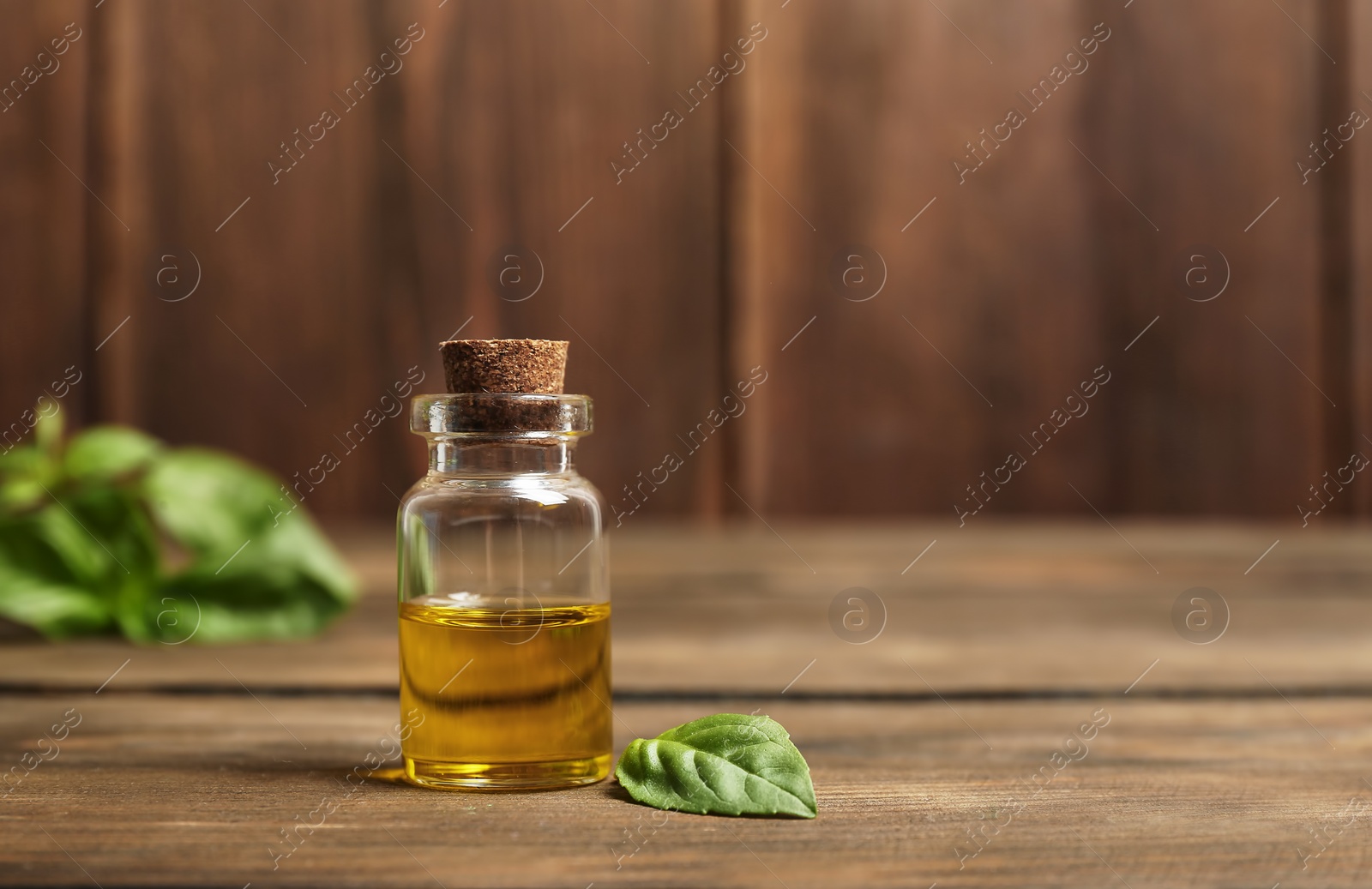 Photo of Glass bottle of basil oil and leaf on wooden table. Space for text