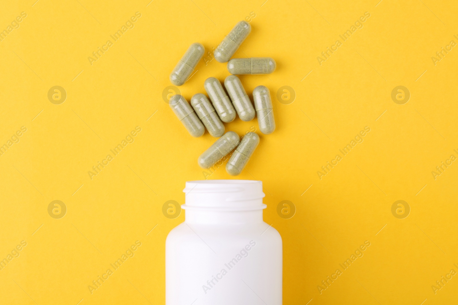 Photo of Bottle and vitamin capsules on yellow background, top view