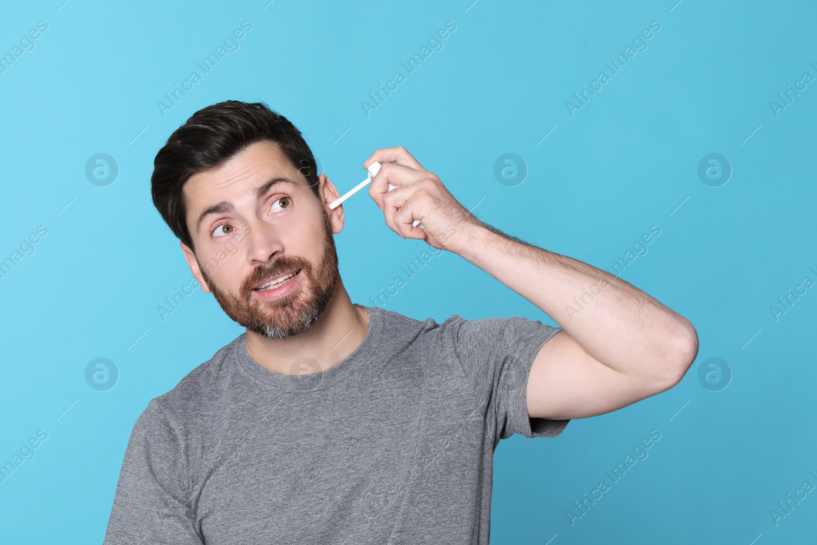 Photo of Man using ear spray on light blue background