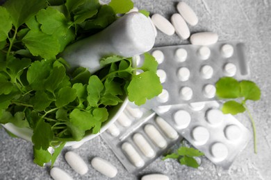 Photo of Mortar with fresh green celandine and pills on light grey table, top view