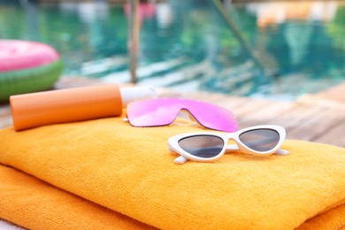 Photo of Sunglasses and sunscreen on beach towel near outdoor swimming pool at luxury resort, closeup. Space for text