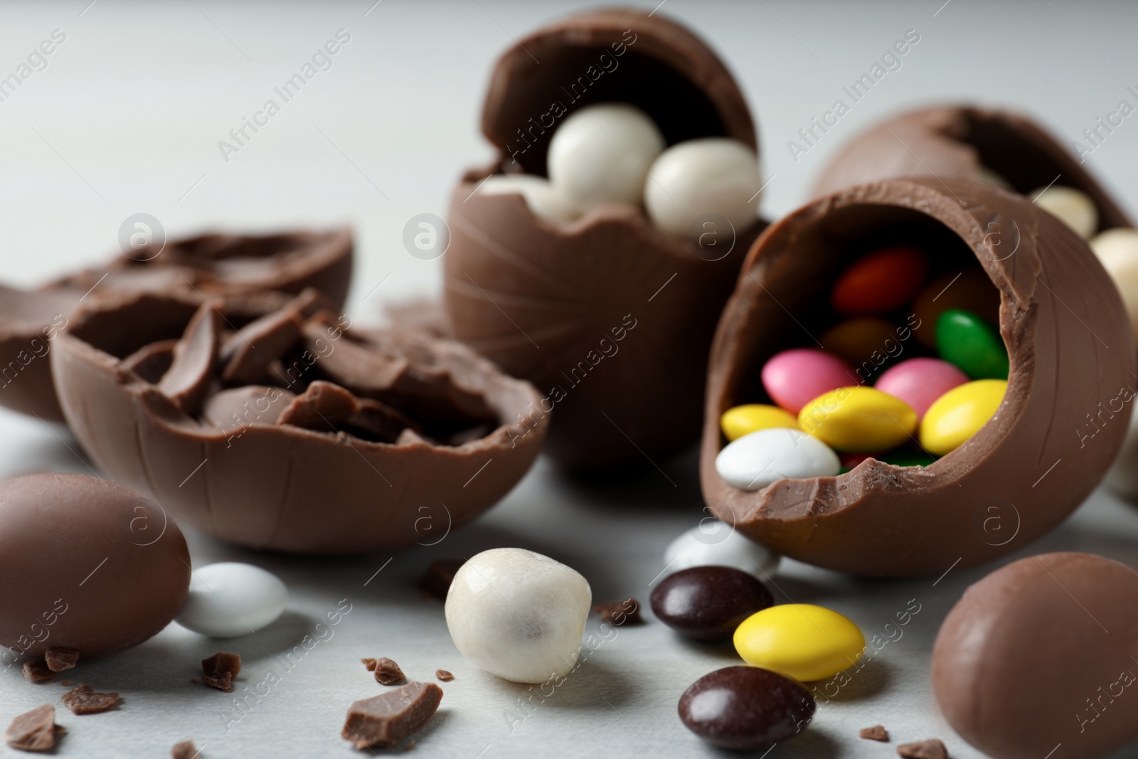 Photo of Broken chocolate eggs with candies on white wooden table, closeup