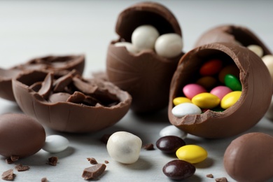 Photo of Broken chocolate eggs with candies on white wooden table, closeup