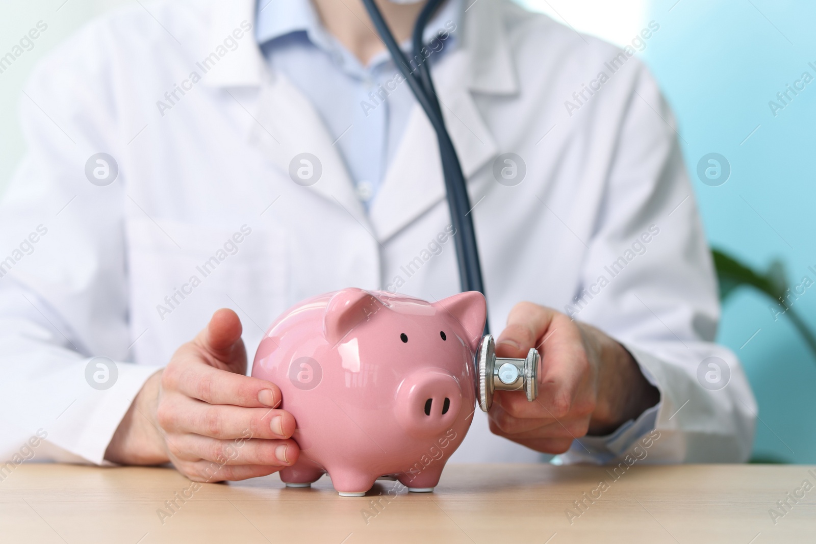 Doctor with piggy bank and stethoscope at wooden table, closeup Photo of Doctor with piggy bank and stethoscope at wooden table, closeup