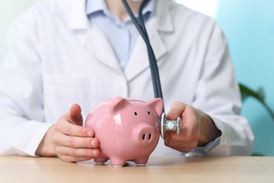 Photo of Doctor with piggy bank and stethoscope at wooden table, closeup