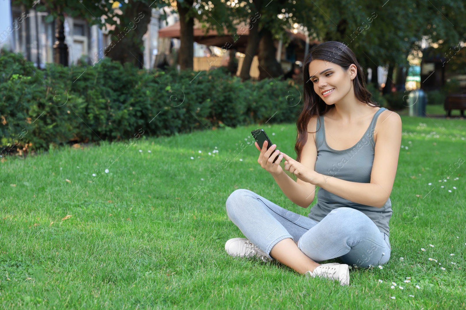 Photo of Young woman using smartphone on green grass in park