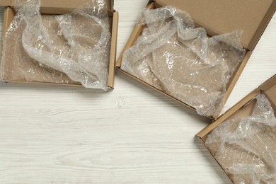 Photo of Open cardboard boxes with bubble wrap on white wooden background, flat lay. Space for text