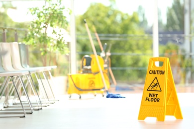 Photo of Safety sign with phrase Caution wet floor and blurred mop bucket on background. Cleaning service