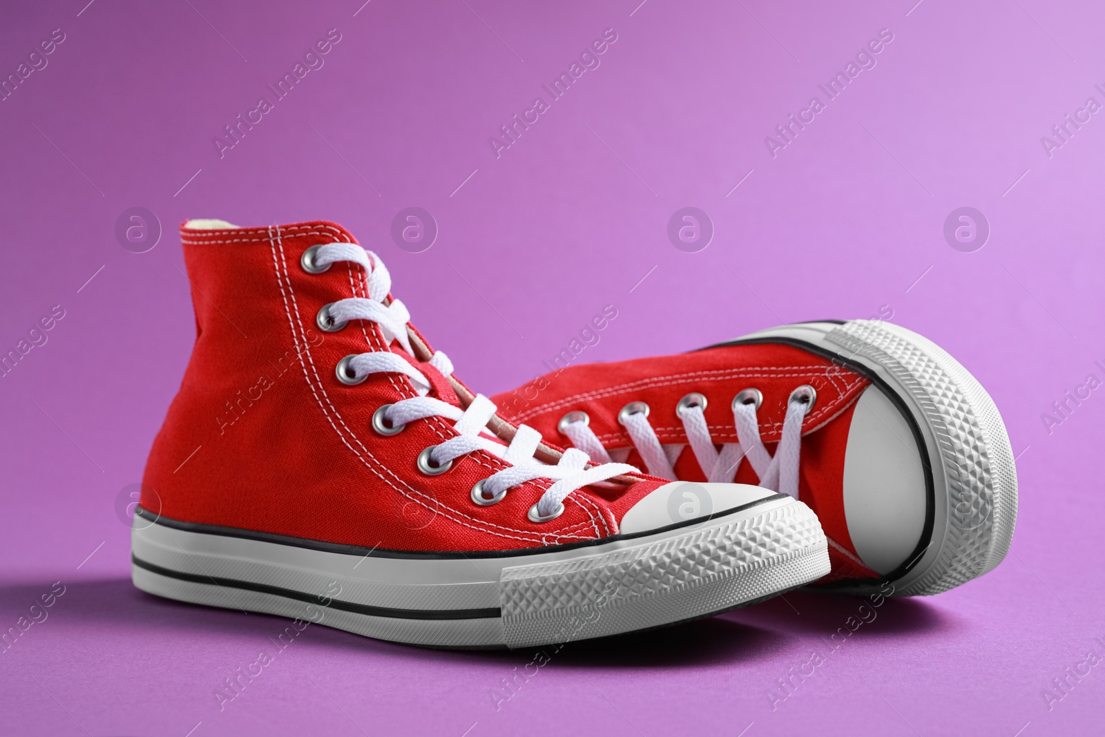 Photo of Pair of new stylish red sneakers on purple background