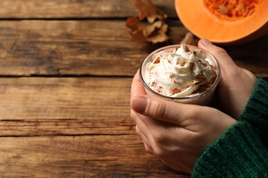 Photo of Woman holding tasty pumpkin latte at wooden table, closeup. Space for text