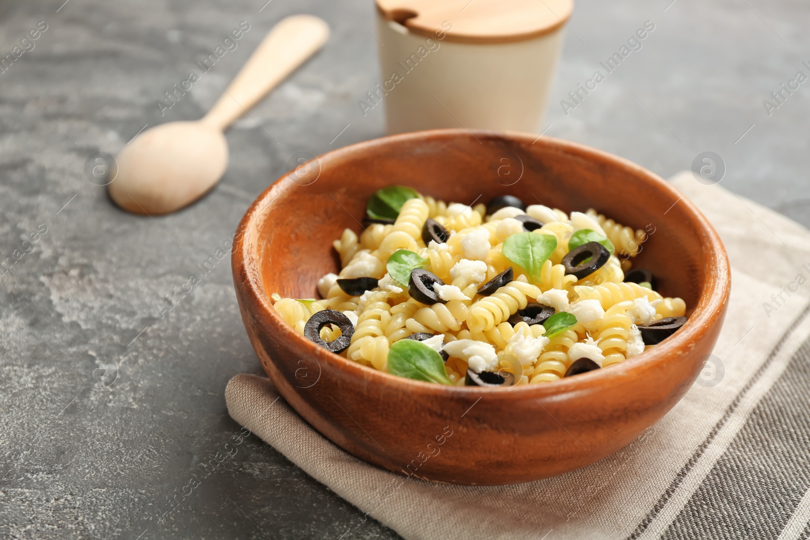 Photo of Wooden bowl with delicious pasta salad on grey background