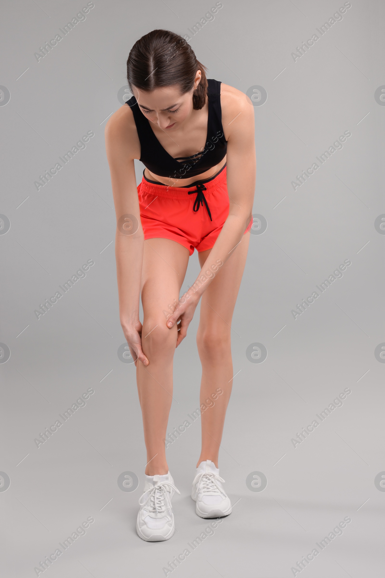 Photo of Young woman suffering from leg pain on grey background