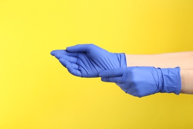 Person putting on medical gloves against yellow background, closeup of hands