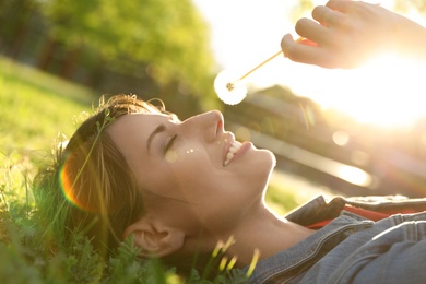 Young woman with dandelion in park on sunny day. Allergy free concept