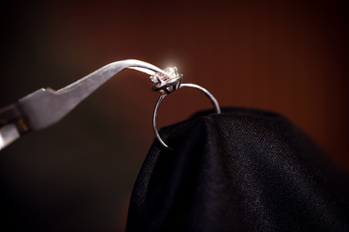 Photo of Working with beautiful ring on dark background, closeup. Jeweler's workshop