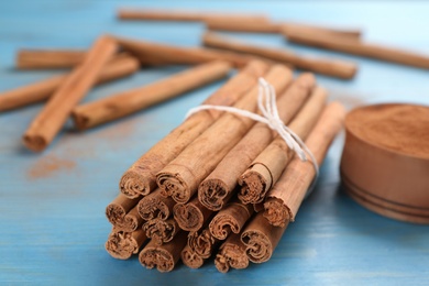 Photo of Aromatic cinnamon sticks on light blue wooden table, closeup