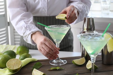 Bartender squeezing lime juice into glass with delicious Margarita cocktail at wooden table, closeup