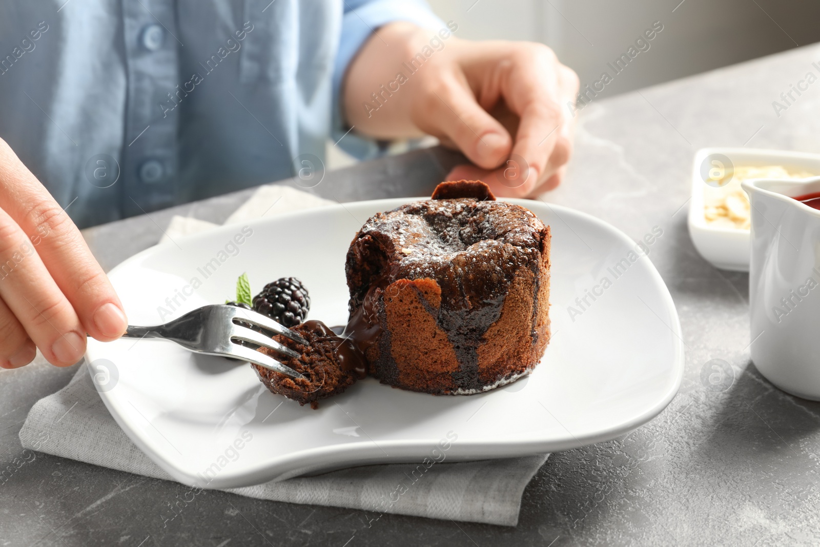 Photo of Woman eating delicious fresh fondant with hot chocolate at table. Lava cake recipe