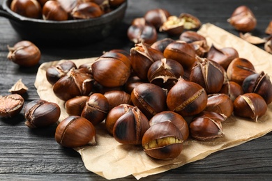 Photo of Tasty roasted edible chestnuts on black wooden table, closeup