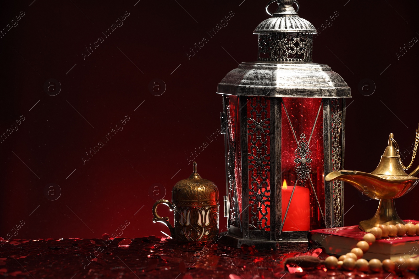 Photo of Arabic lantern, Quran, misbaha and Aladdin magic lamp on shiny red table. Space for text