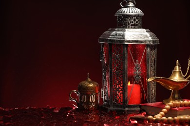 Photo of Arabic lantern, Quran, misbaha and Aladdin magic lamp on shiny red table. Space for text