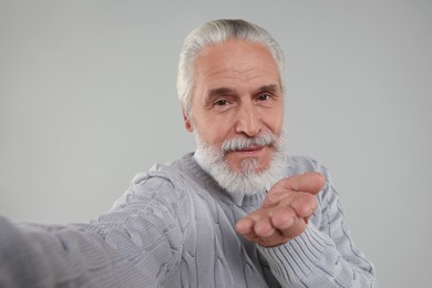 Photo of Senior man taking selfie and blowing kiss on light grey background