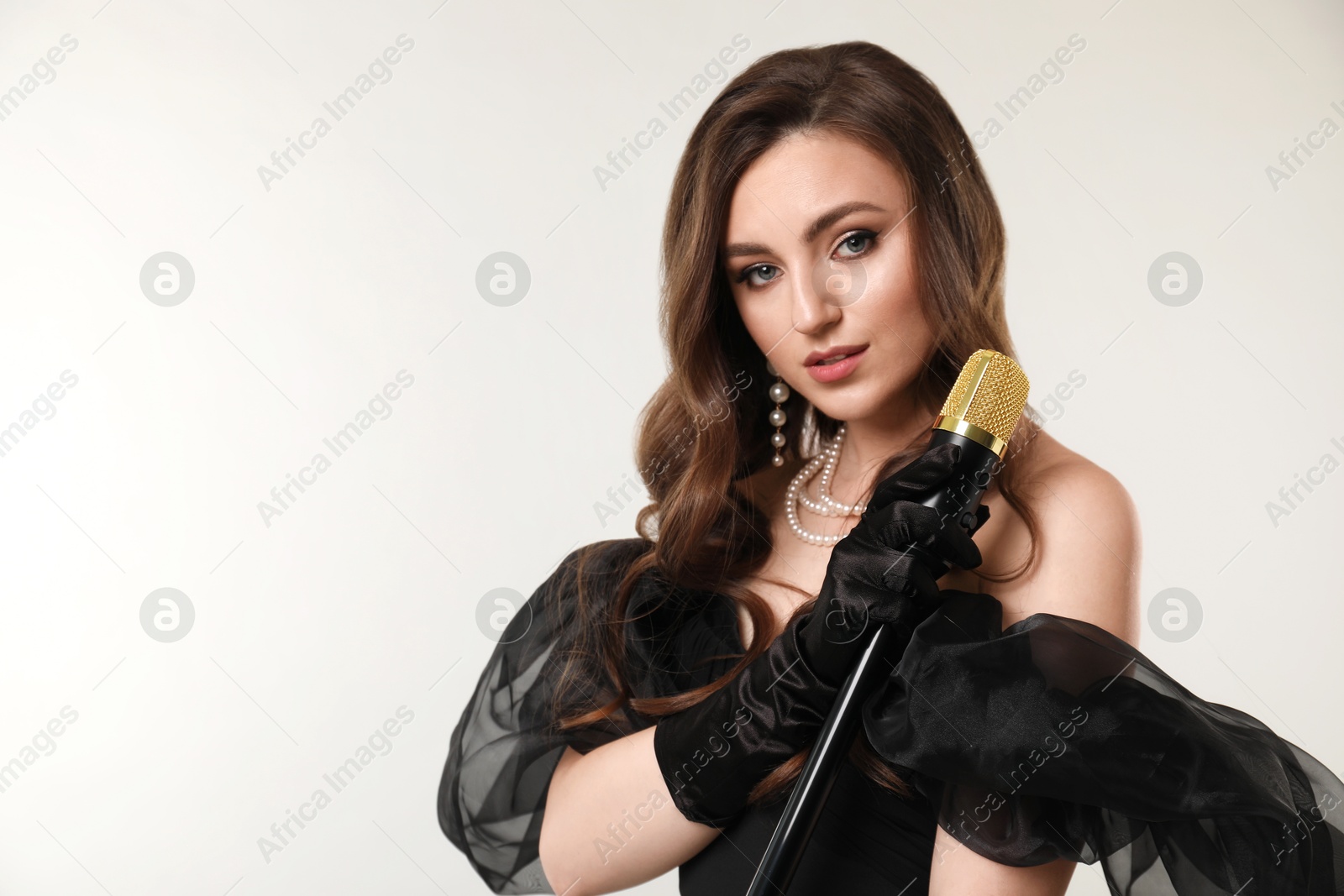Photo of Beautiful young jazz singer with microphone on light grey background, space for text
