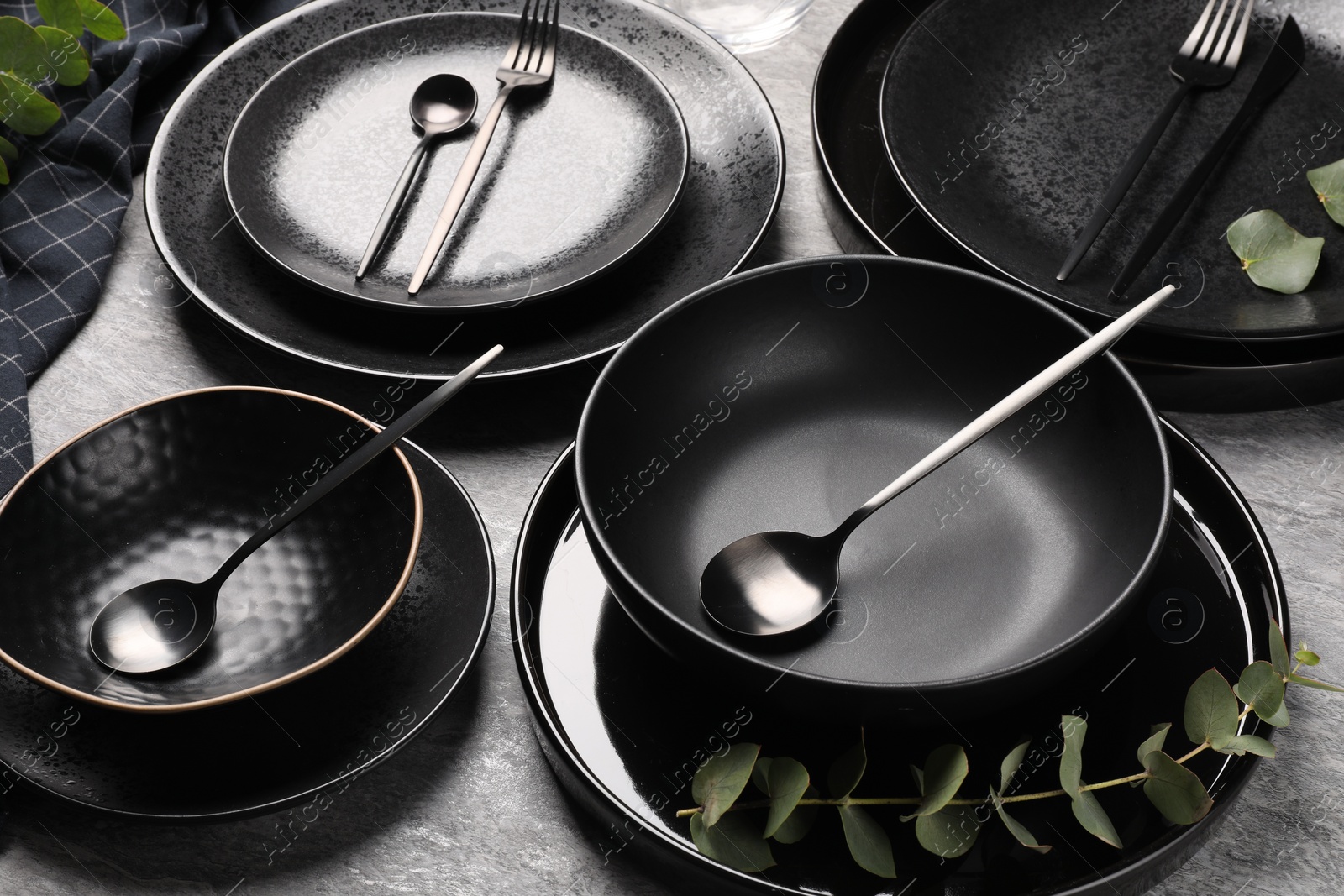 Photo of Stylish table setting. Dishes, cutlery and eucalyptus branch on grey surface