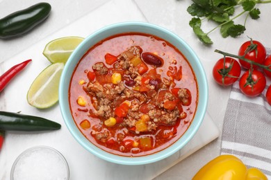 Photo of Bowl with tasty chili con carne and ingredients on white table, flat lay
