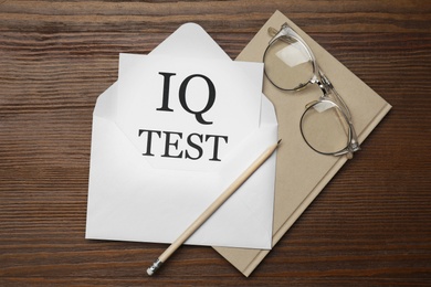 Photo of Paper with words IQ Test in envelope, pencil, notebook and glasses on wooden table, flat lay