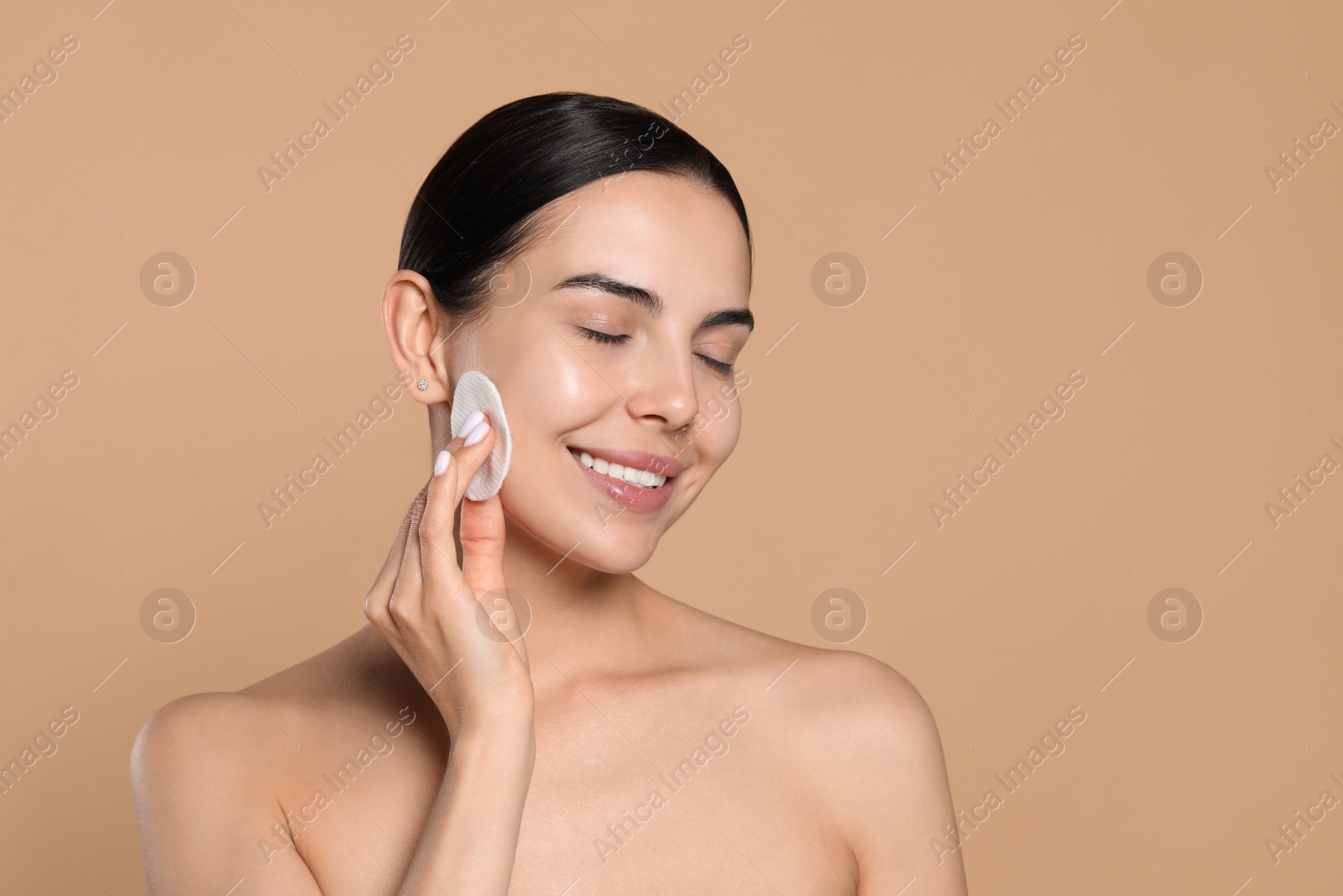 Photo of Young woman using cotton pad with micellar water on beige background, space for text