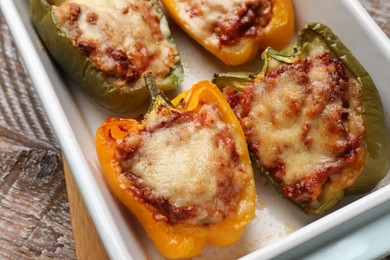 Photo of Tasty stuffed peppers in dish on wooden table, closeup