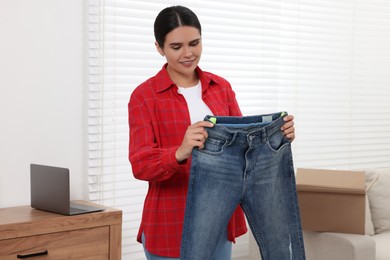 Photo of Young woman with just unpacked new jeans at home. Online shopping