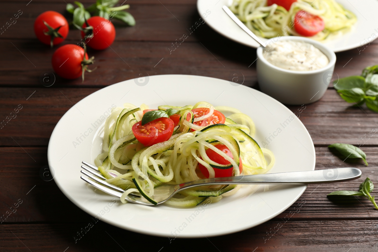 Photo of Tasty zucchini pasta with tomatoes and basil served on wooden table