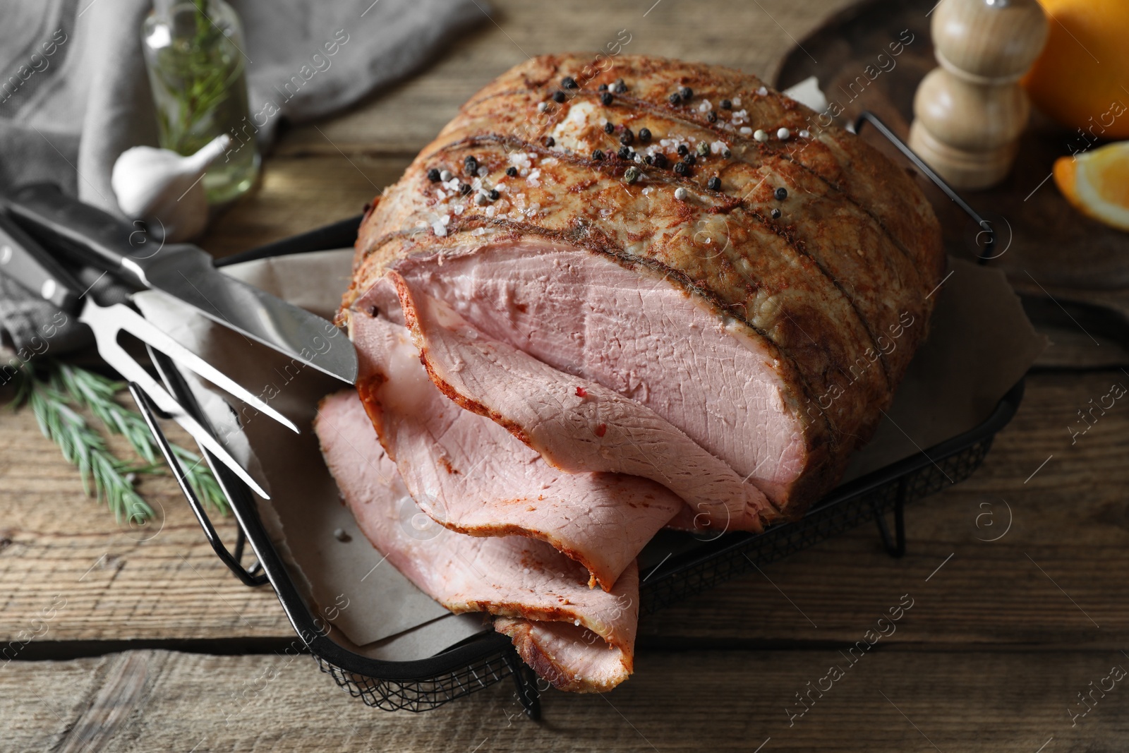 Photo of Delicious baked ham, carving fork, knife and rosemary on wooden table